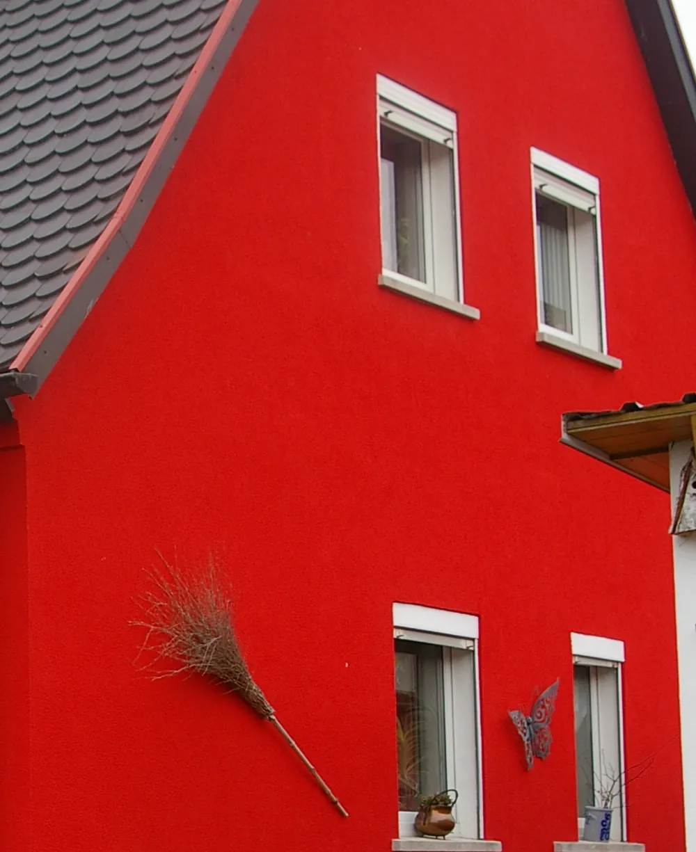 Giebelseite eines Wohnhauses mit kräftig roter Fassade und weißen Fensterfaschen